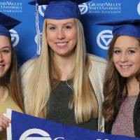 Three graduates pose with GV flag at Gradfest